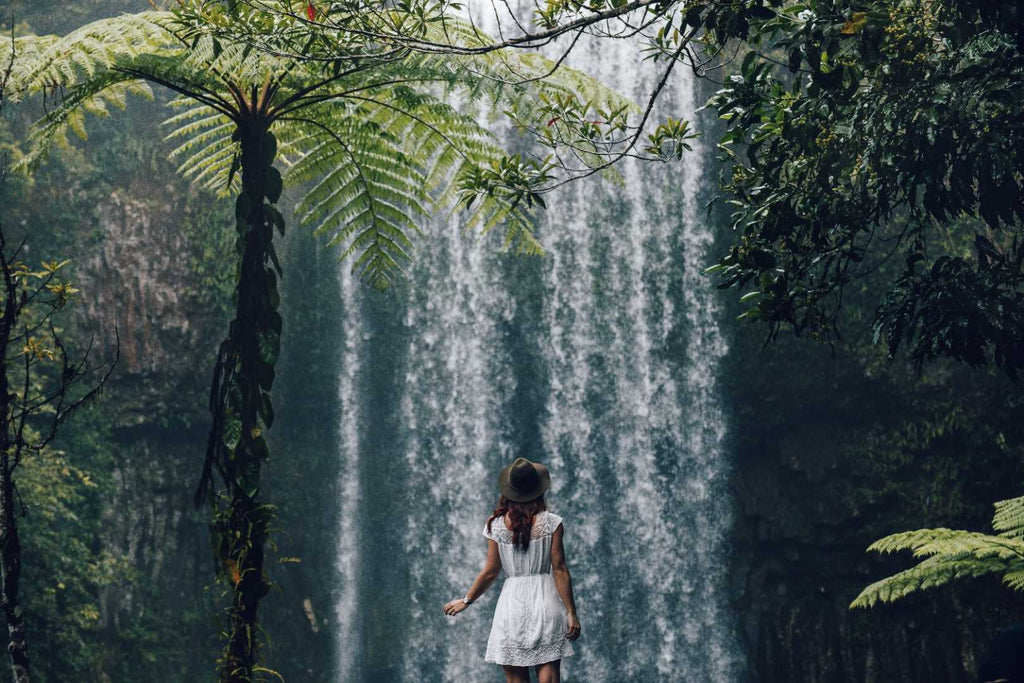 Woman explores lush rainforest waterfall on Whitsundays Reef Tour from Brisbane to Cairns. Scenic stop on small group adventure trip.