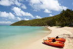 Two kayaks rest on a tropical beach in the Whitsundays, part of the Brisbane to Cairns Reef Tour. Ideal for ocean activities and leisure.