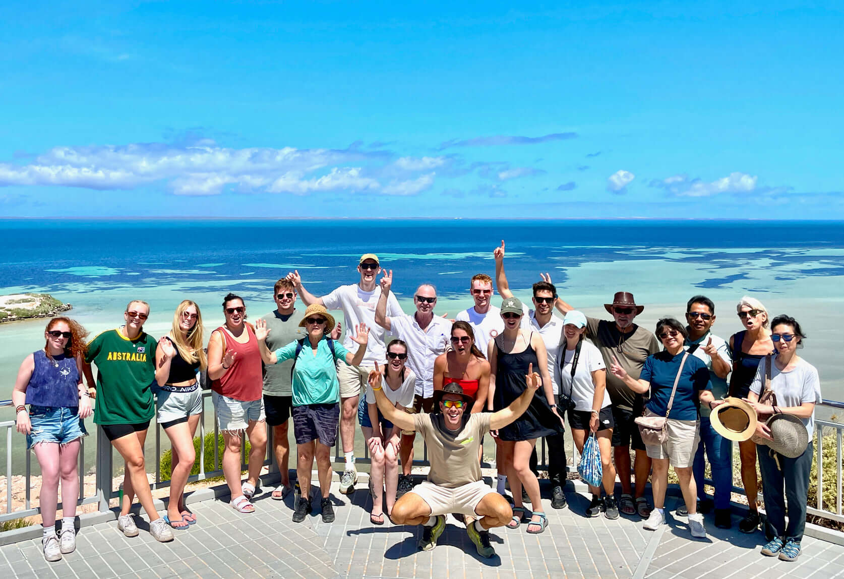 Tour group posing at scenic lookout over Shark Bay during West Coast Road Trip. Group travel experience in Western Australia.