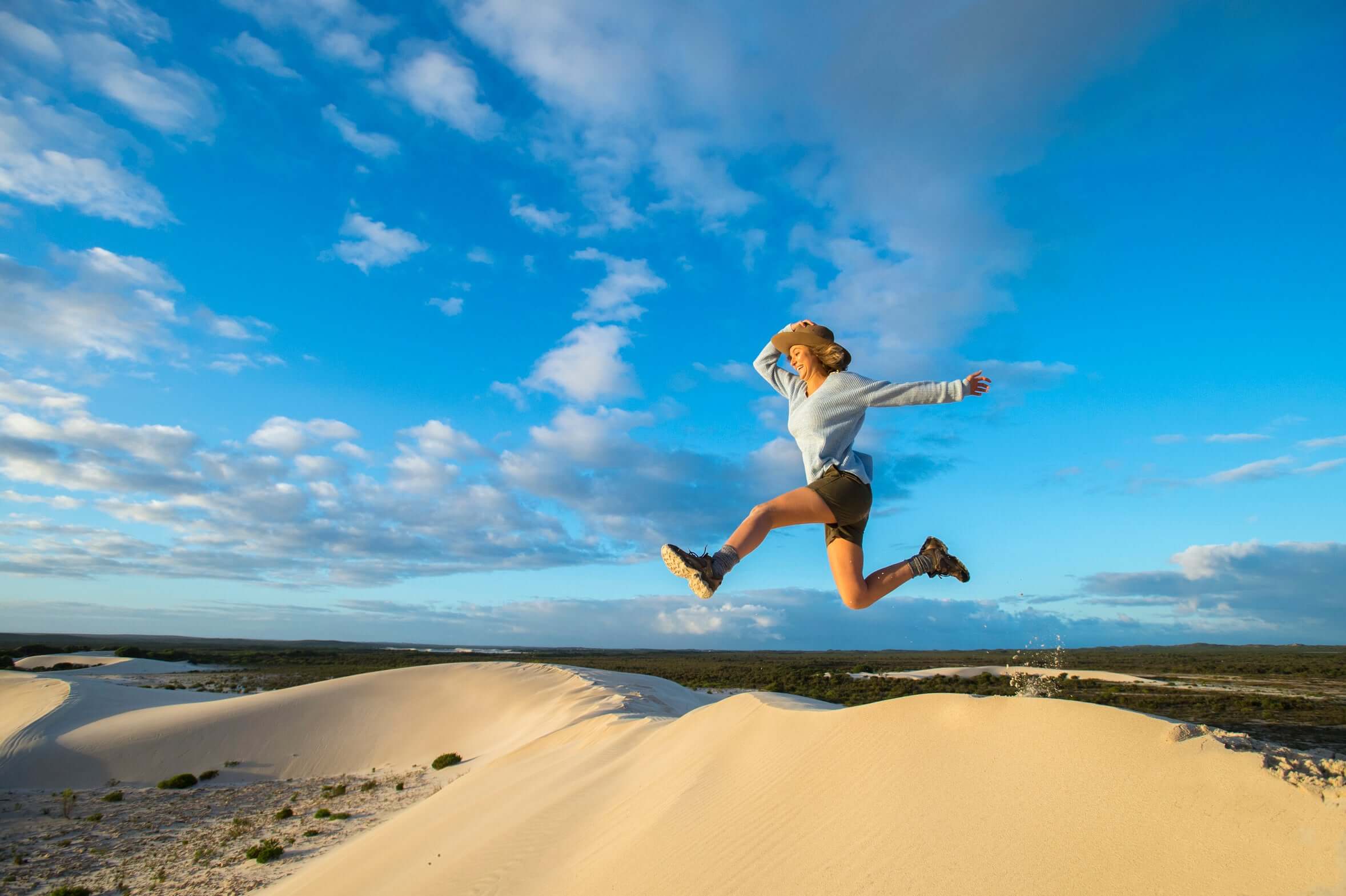 Woman jumping on sand dunes under blue sky during West Coast Road Trip from Perth to Exmouth. Outdoor fun in Pinnacles Desert.