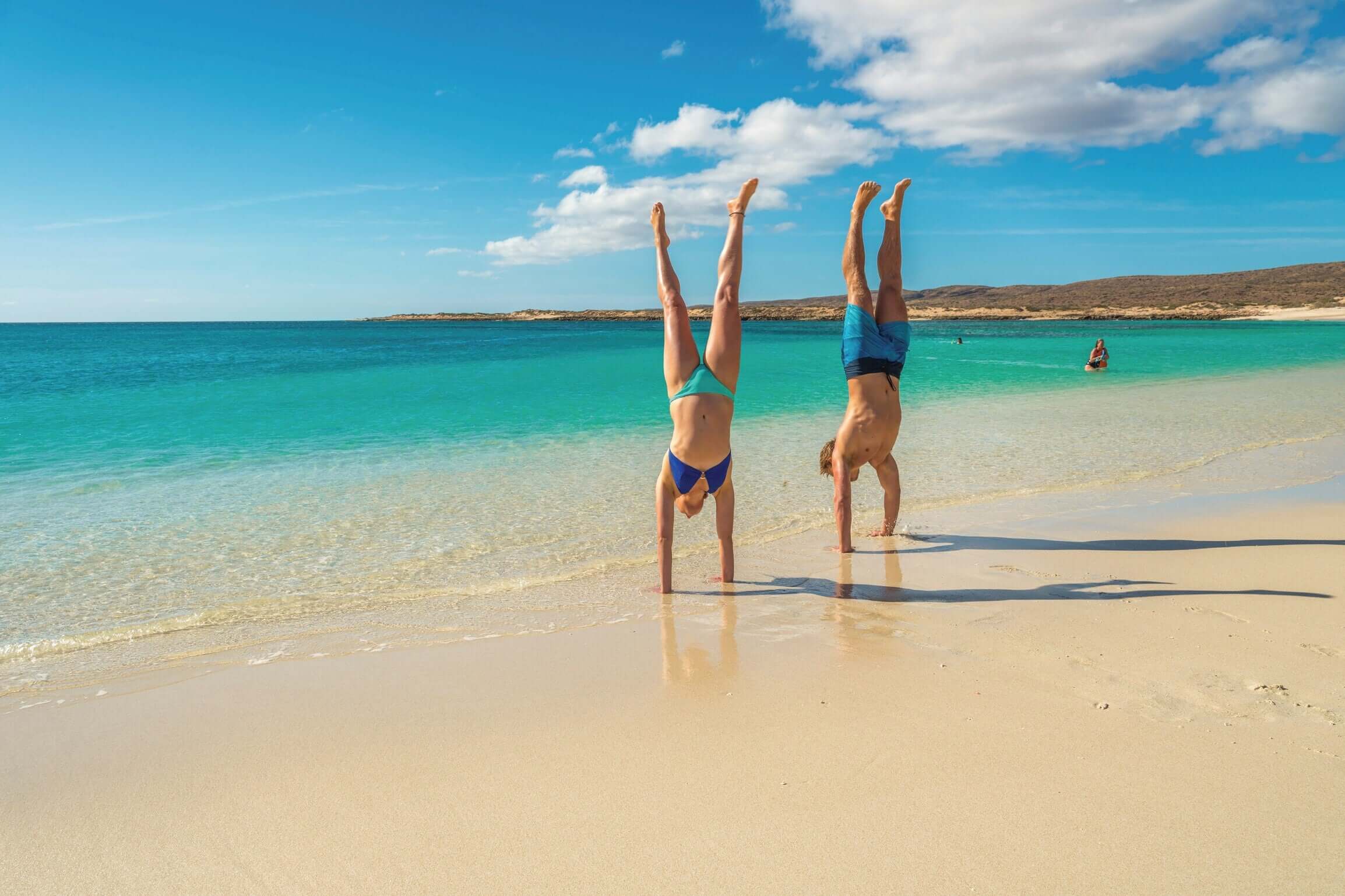 Couple doing handstands on white sand beach at Coral Bay during West Coast Road Trip. Fun beach activity in Western Australia.