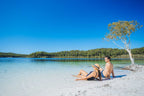 Couple relaxing by Lake McKenzie on K'gari during East Coast Australia tour. Leisure stop on 8-day Sydney to Brisbane journey.