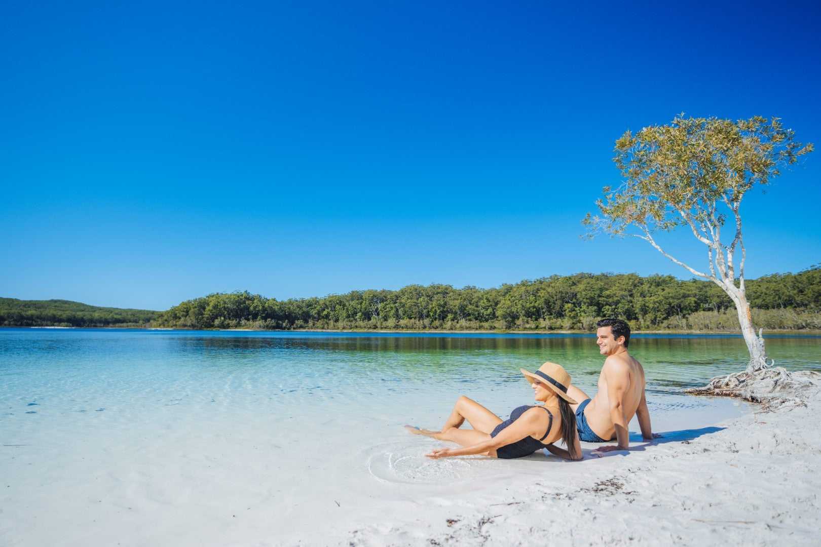 Couple relaxing by Lake McKenzie on K'gari during East Coast Australia tour. Leisure stop on 8-day Sydney to Brisbane journey.
