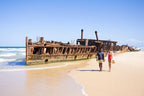 Couple walking past Maheno Shipwreck on K'gari, featured on East Coast Australia tour. Historic site on 8-day Sydney to Brisbane trip.