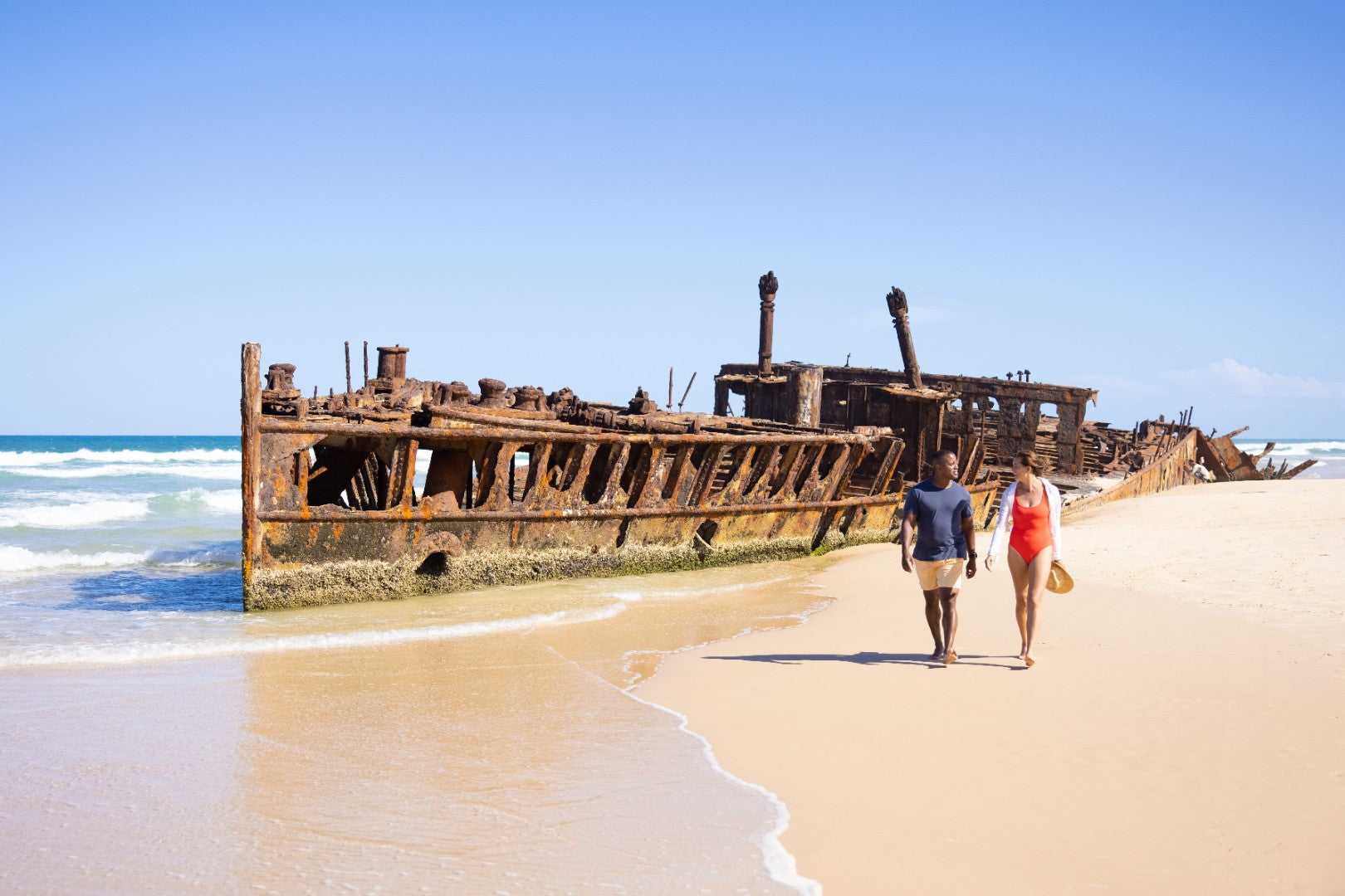 Couple walking past Maheno Shipwreck on K'gari, featured on East Coast Australia tour. Historic site on 8-day Sydney to Brisbane trip.