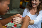 Monk ties a red blessing bracelet on a tourist’s wrist, a cultural ritual on the Angkor to Islands 16-Day Tour - Khmer Culture to Thai Coasts.