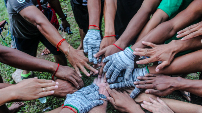 Hands stacked in unity with red bracelets, symbolizing group spirit on the Angkor to Islands 16-Day Tour - Khmer Culture to Thai Coasts.