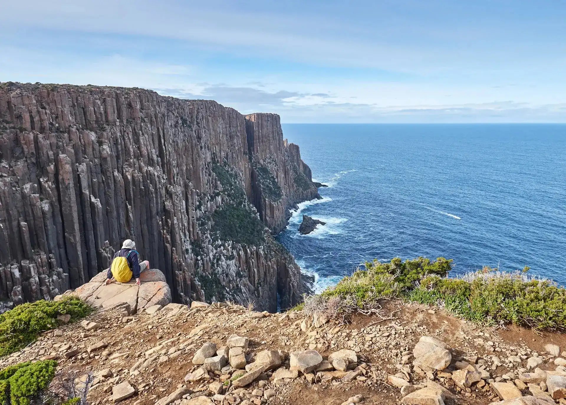 Person standing on a cliff overlooking the ocean with a clear blue sky.