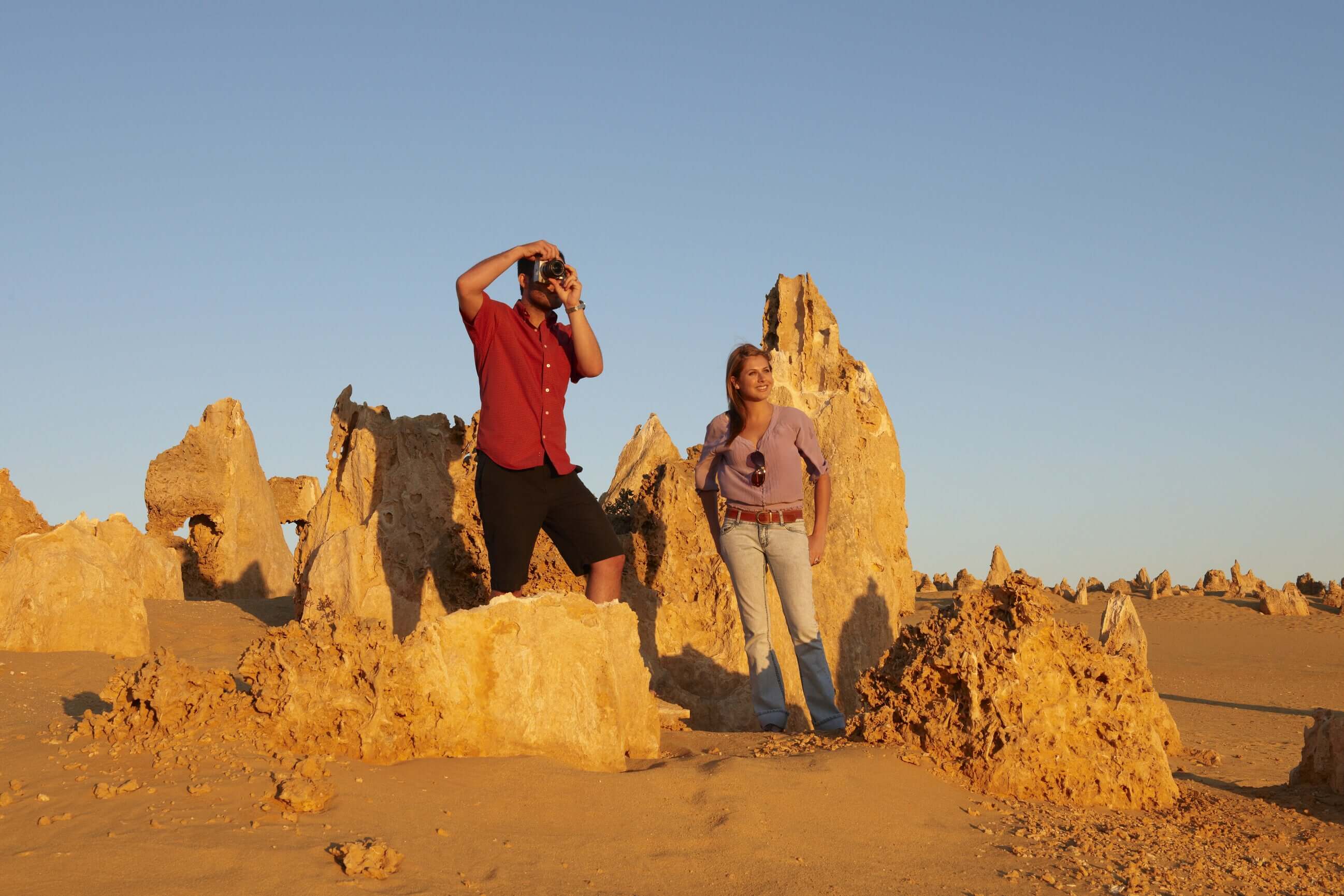 Couple photographing Pinnacles Desert rock formations during West Coast Road Trip. Iconic natural attraction in Western Australia.