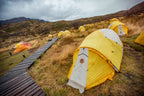 Yellow tents set up in a grassy field with mountains in the background