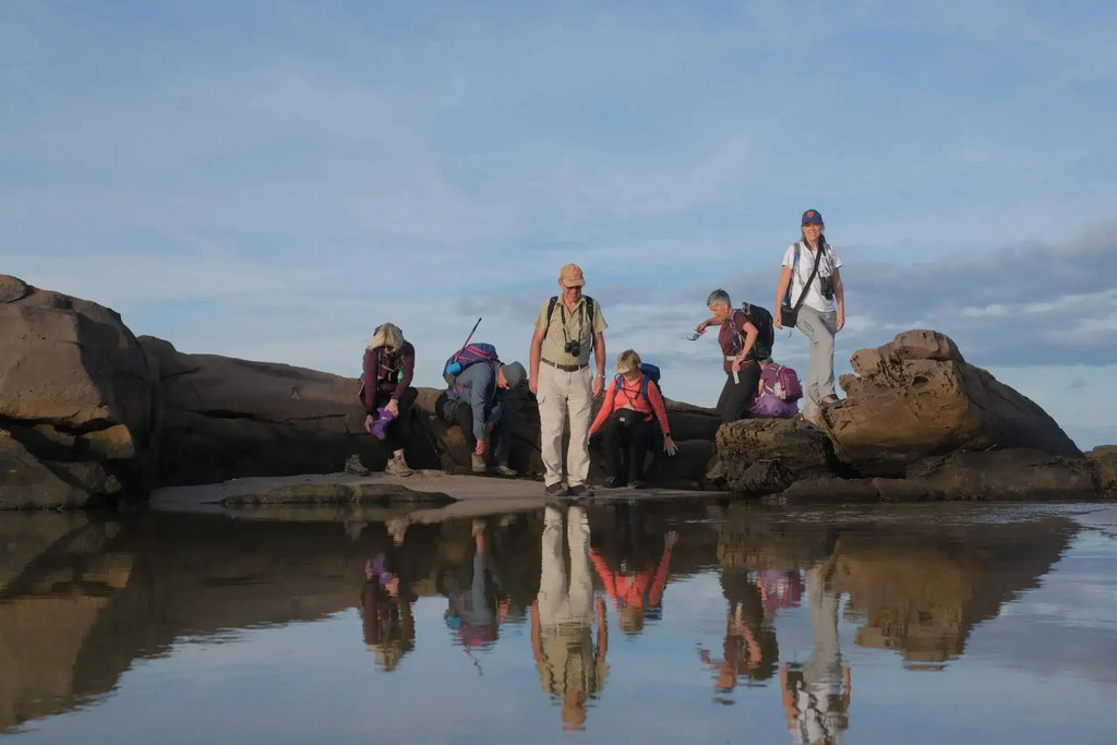 Group of people standing on rocks with their reflections in the water below.