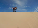 Two hikers celebrating atop a sand dune under a blue sky during an adventurous outdoor trek.