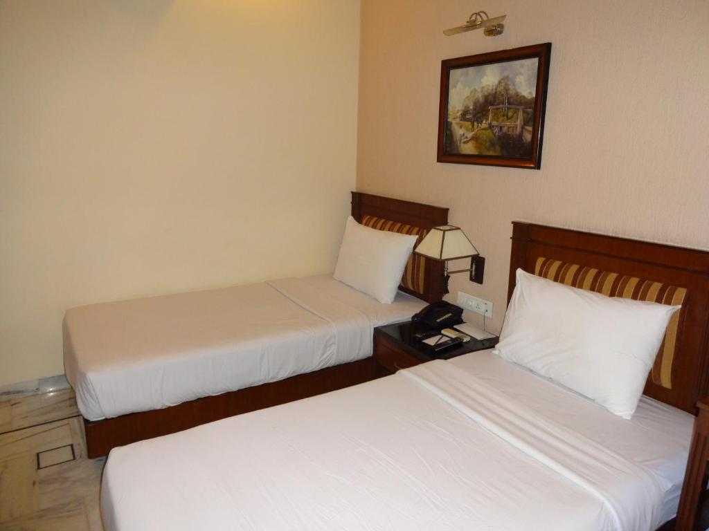 Two beds in a room with a nightstand and lamp on a beige wall.