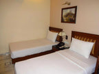 Two beds in a room with a nightstand and lamp on a beige wall.