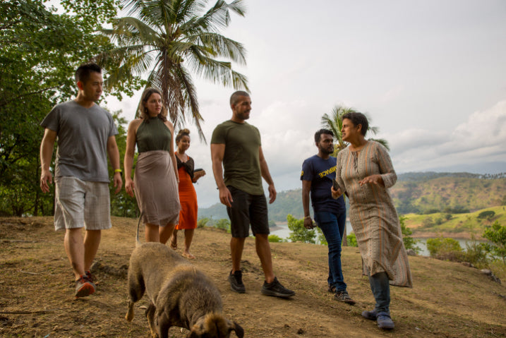 Travelers hiking through rural Sri Lankan landscape with local guide and dog. Explore Sri Lanka - Land & Sea Tour Options offers immersive land tours.