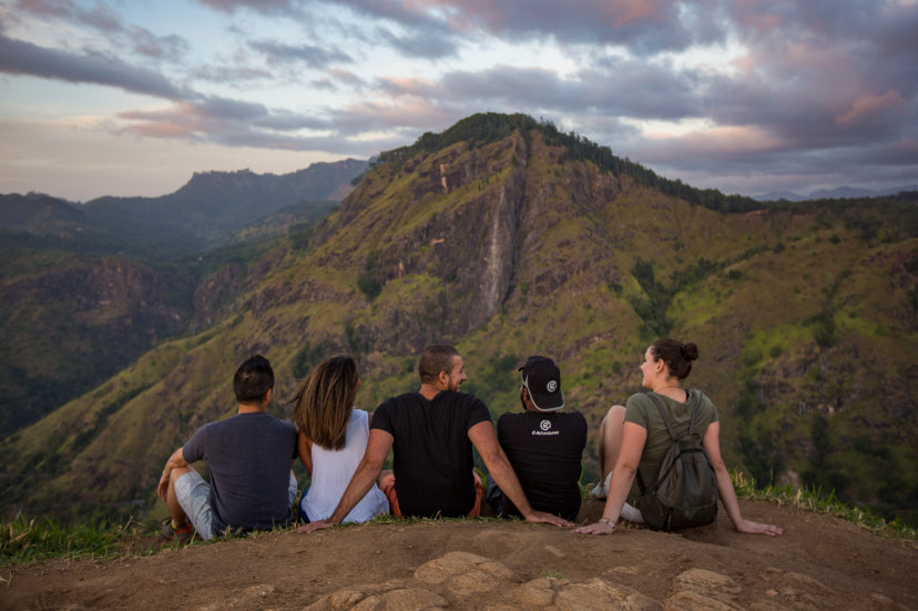 Travelers sitting on hilltop overlooking Ella Rock at sunset. Explore Sri Lanka - Land & Sea Tour Options features breathtaking mountain views.