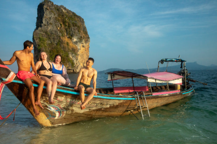 Group of friends on a longtail boat near Thai limestone cliffs, part of the island adventures on the Angkor to Islands 16-Day Tour - Khmer Culture to Thai Coasts.