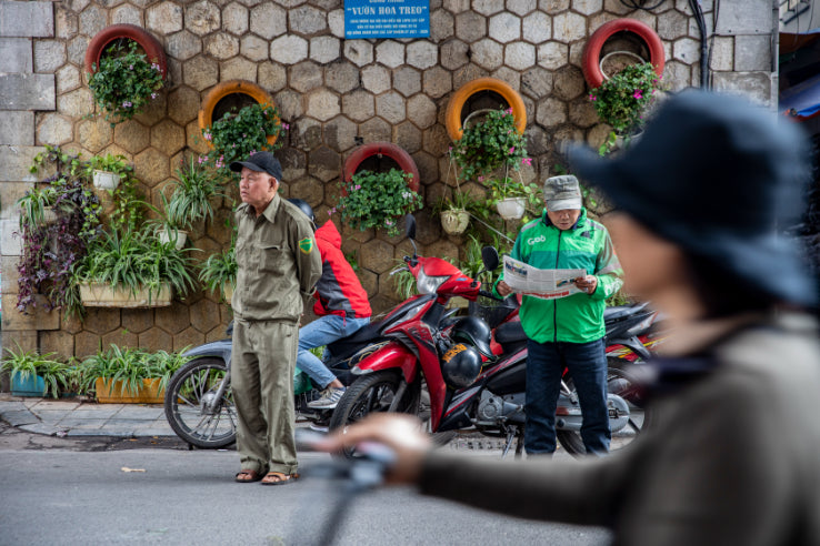 Vietnamese locals reading and relaxing near motorbikes on a street. Captures daily life during Vietnam Hiking and Cycling Tour.