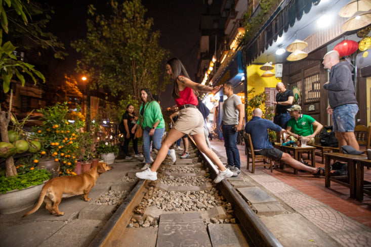 Tourist walking along Hanoi's famous train street lined with cafes. Urban exploration on Vietnam Hiking and Cycling Tour itinerary.