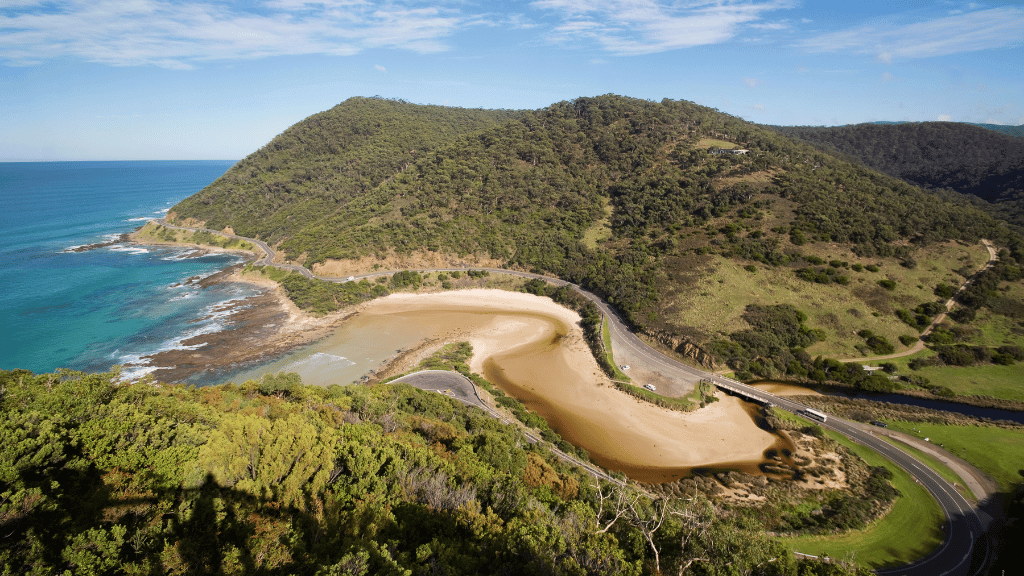 Breathtaking view of Victoria's coastline, featuring lush hills and a serene beach on the Great Ocean Walk.