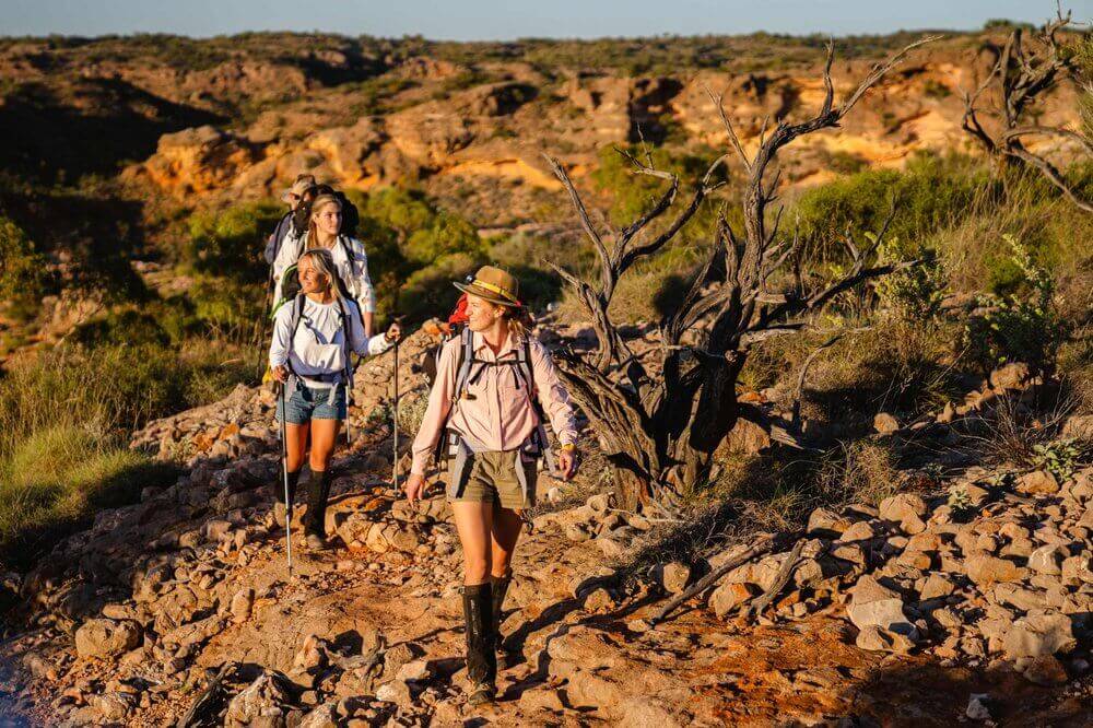 Three adventurers hiking through rugged terrain in Cape Range, enjoying an all-inclusive outdoor trek experience.