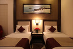 Two beds in a hotel room with a painting on the wall above.