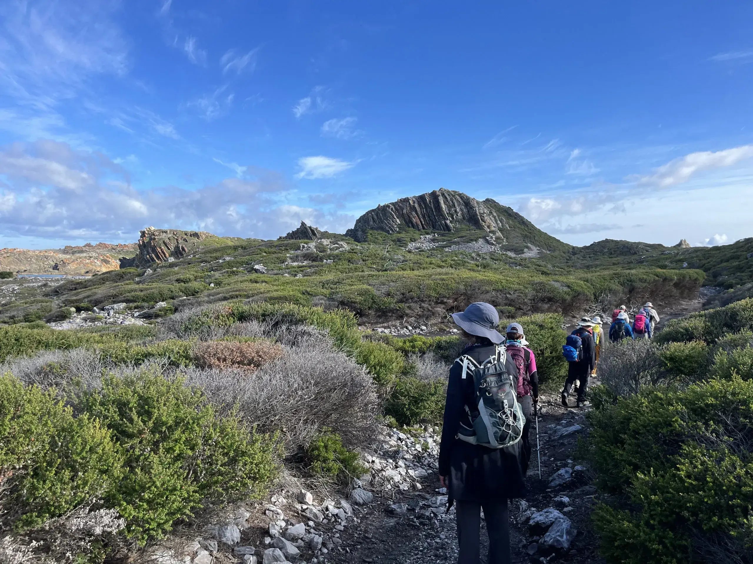 Group of people hiking on a trail with scenic landscape and blue sky.