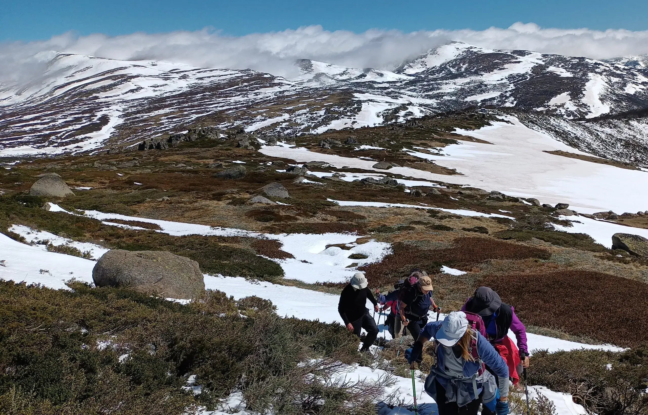 Hikers on a mountain trail with snow and rocky terrain