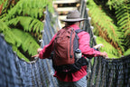 Person with a red jacket and backpack crossing a suspension bridge in a forest