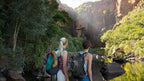 Two hikers admiring waterfall view at Kakadu Litchfield Camping Adventure - 3-Day Tour. Scenic bushwalk with towering cliffs and water.