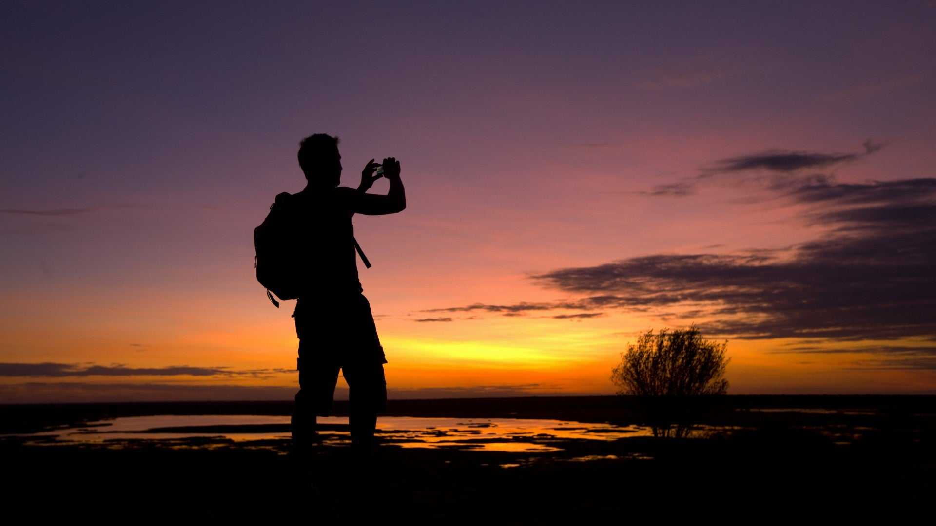 Silhouette of man photographing sunset over wetlands on Kakadu Katherine Gorge Tour | 4-Day Comfort Travel. Capturing scenic outback views.
