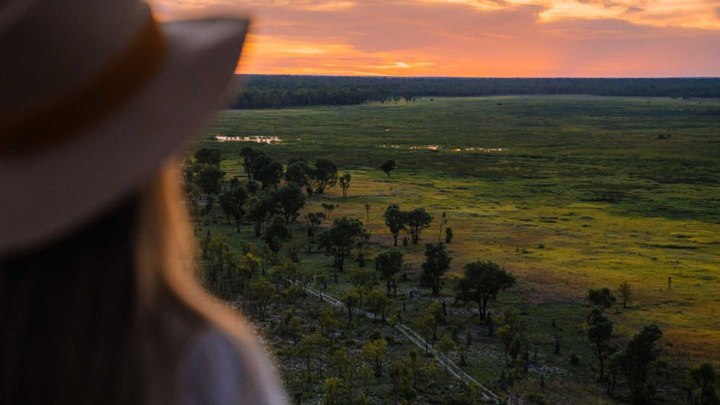 Sunset over wetlands viewed by traveler at Kakadu Litchfield Camping Adventure - 3-Day Tour. Vibrant sky and expansive green floodplain.