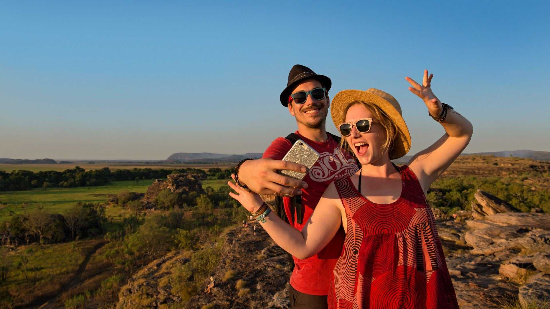 Couple taking selfie at scenic lookout during Kakadu Litchfield Camping Adventure - 3-Day Tour. Sunset over vast outback landscape.