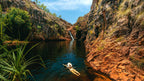 Traveler floating in plunge pool beneath waterfall at Kakadu Litchfield Camping Adventure - 3-Day Tour. Peaceful gorge with red rock walls.