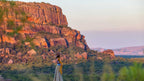 Traveler walking near sandstone cliffs at sunset during Kakadu Litchfield Camping Adventure - 3-Day Tour. Vibrant outback landscape and rock formations.