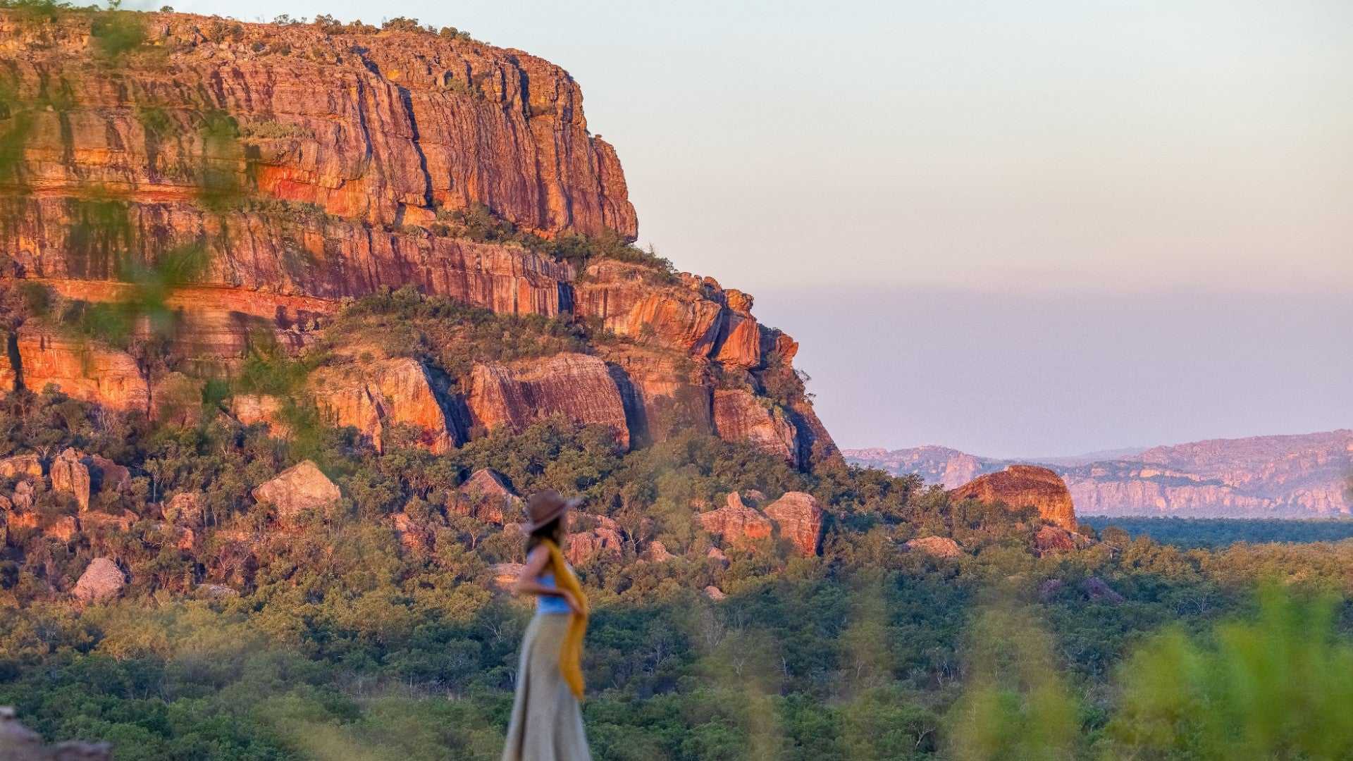 Traveler walking near sandstone cliffs at sunset during Kakadu Litchfield Camping Adventure - 3-Day Tour. Vibrant outback landscape and rock formations.