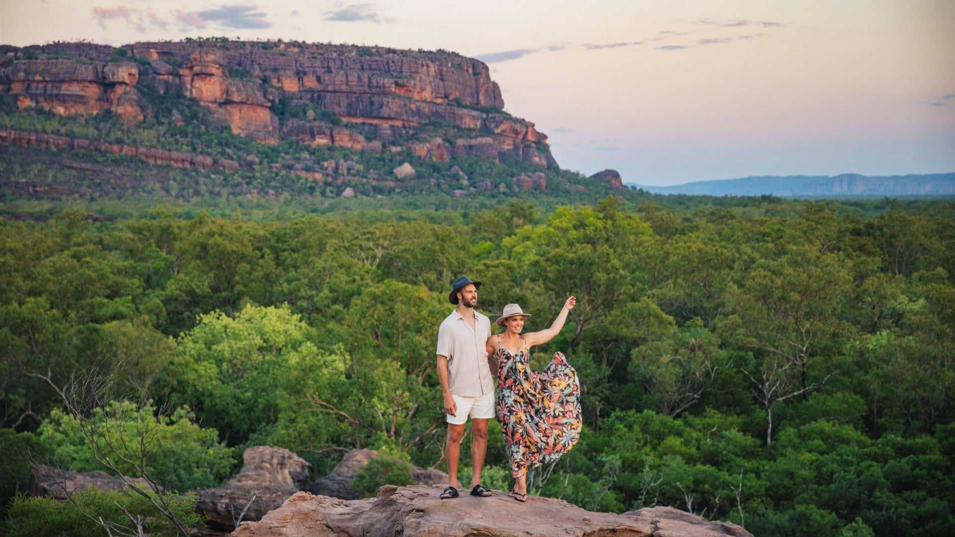 Couple admiring panoramic escarpment views during Kakadu Litchfield Camping Adventure - 3-Day Tour. Vast green forest and sandstone cliffs at sunset.