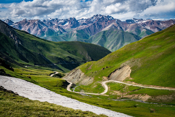 Winding mountain road through lush green valleys in Kyrgyzstan, a scenic drive on the 14-23 Day Central Asia Silk Road Tour.