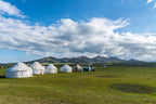 Cluster of yurts in a green Kyrgyz pasture, offering authentic nomadic stays on the 14-23 Day Central Asia Silk Road Tour.