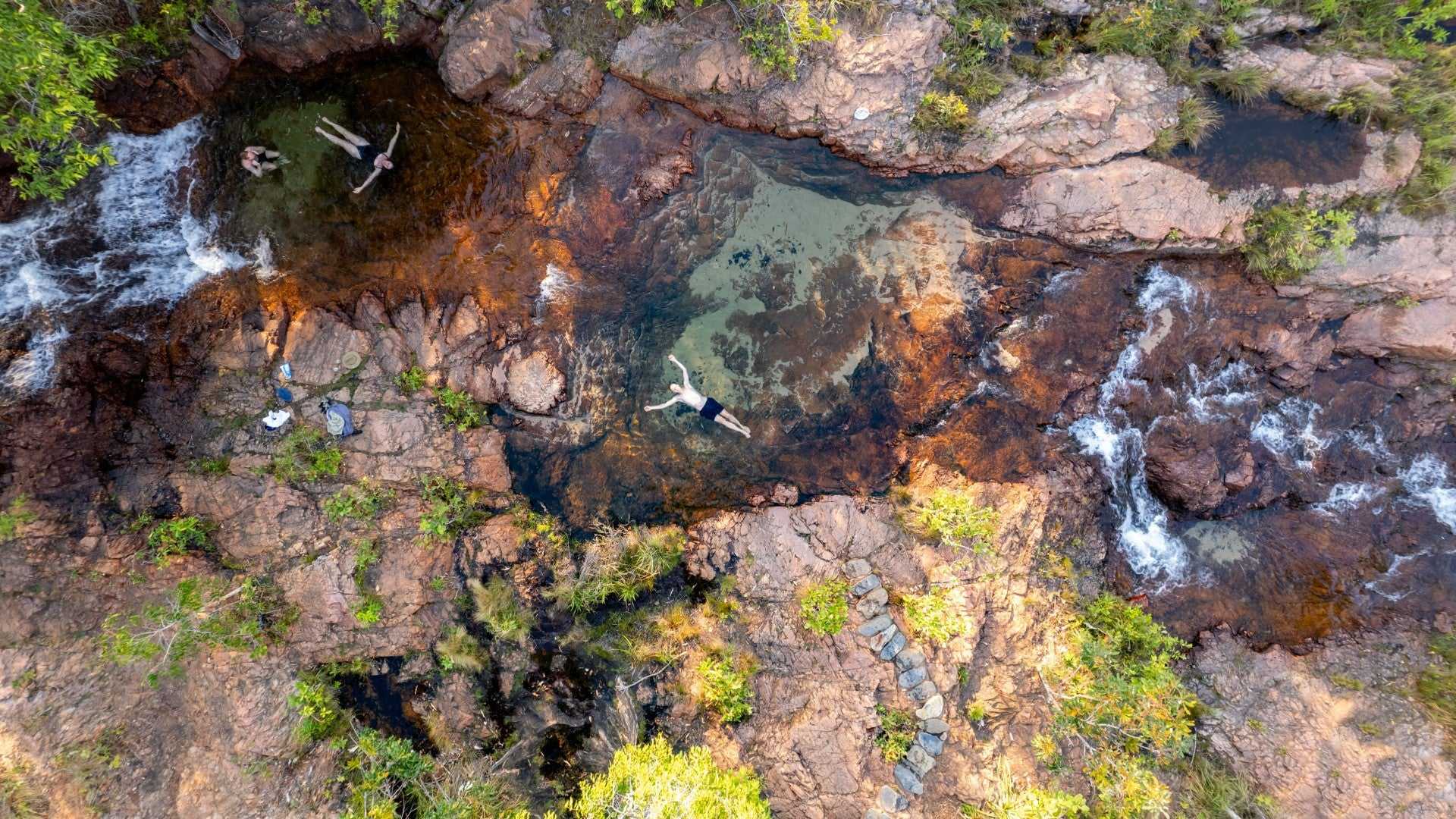 Aerial view of travelers relaxing in rock pools at Kakadu Litchfield Camping Adventure - 3-Day Tour. Clear water streams through rugged terrain.