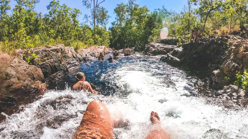 Traveler sliding down natural rock chute at Kakadu Litchfield Camping Adventure - 3-Day Tour. Fun water activity in forest stream.