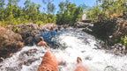 Traveler sliding down natural rock chute at Kakadu Litchfield Camping Adventure - 3-Day Tour. Fun water activity in forest stream.