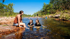 Friends relaxing in shallow rock pool at Kakadu Litchfield Camping Adventure - 3-Day Tour. Clear water and red stone in natural setting.