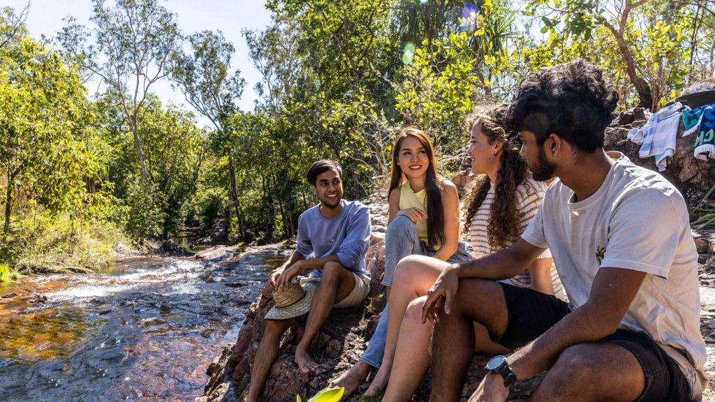 Group of friends relaxing by forest stream at Kakadu Litchfield Camping Adventure - 3-Day Tour. Social moment in lush, shaded environment.