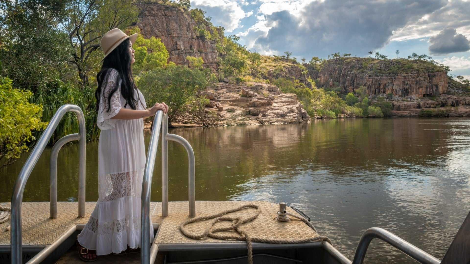 Woman admires Katherine Gorge from boat on Kakadu Katherine Gorge Tour | 4-Day Comfort Travel. Scenic cruise through rocky canyon.