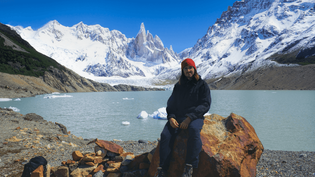 Traveler sitting by glacial lake with snowy peaks in Patagonia on the Blue Heart Adventure | 9 Days. Ideal for hiking, camping, and photography.