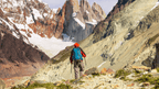 Hiker trekking through rocky terrain toward jagged peaks in Patagonia on the Blue Heart Adventure | 9 Days. Challenging trails and epic views.