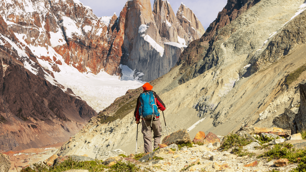 Hiker trekking through rocky terrain toward jagged peaks in Patagonia on the Blue Heart Adventure | 9 Days. Challenging trails and epic views.