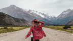 Woman in red flannel walking toward snow-capped mountains in Patagonia, part of the 9-day Blue Heart Adventure hiking tour through Torres del Paine.