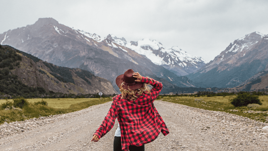 Woman in red flannel walking toward snow-capped mountains in Patagonia, part of the 9-day Blue Heart Adventure hiking tour through Torres del Paine.